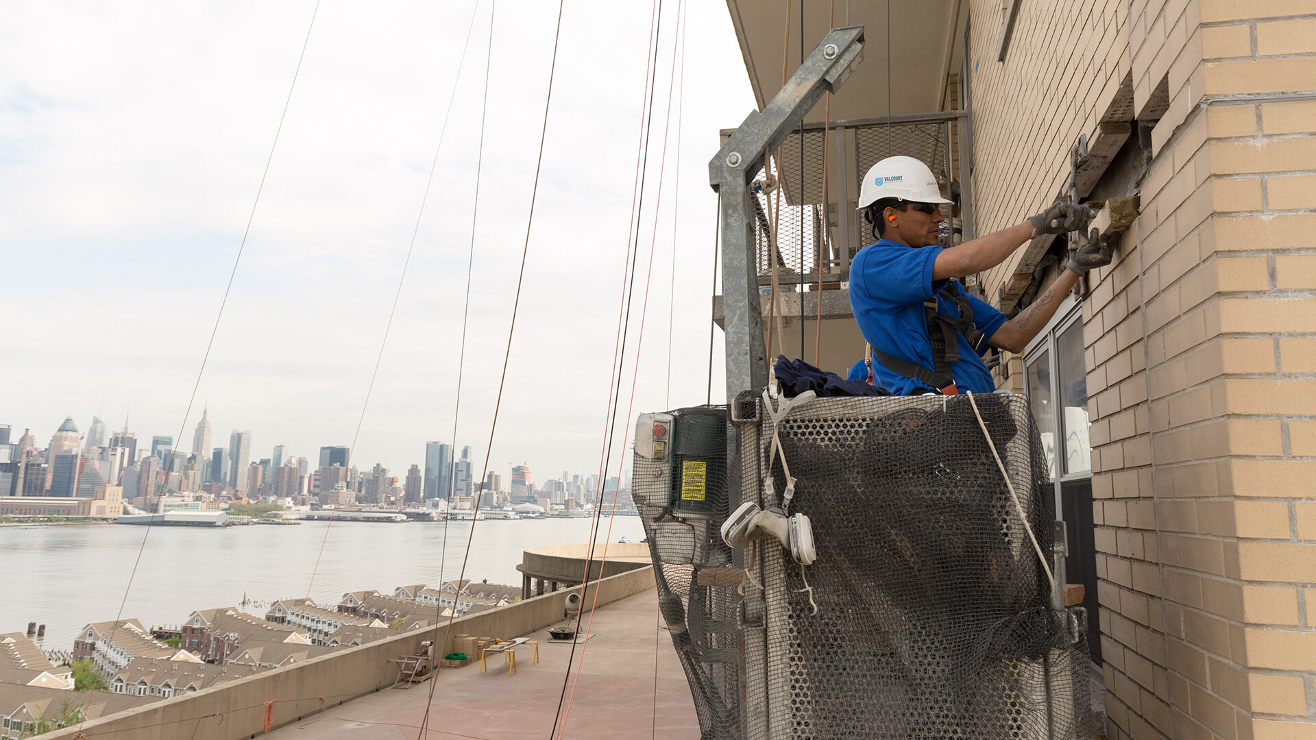 Worker performing facade restoration on a high-rise building with city skyline in background