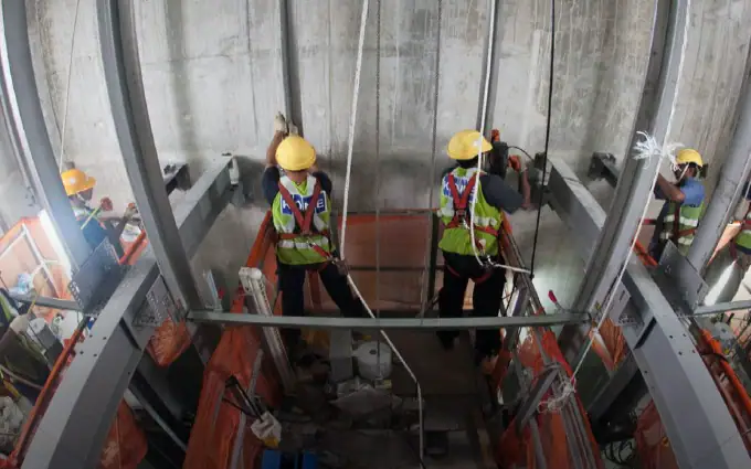 Workers in safety gear installing or maintaining an elevator in a lift shaft