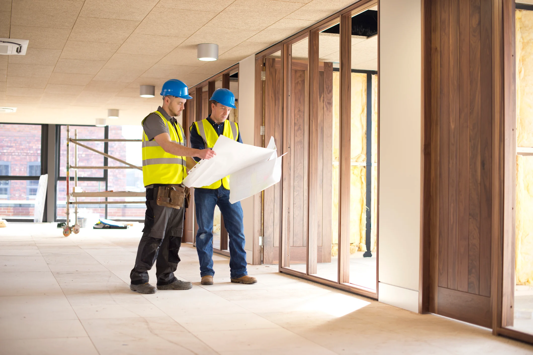 Two construction professionals in hard hats and high-visibility vests examining blueprints at a construction site