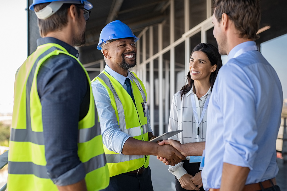 Construction professionals meeting at a building site, with a project manager in safety gear shaking hands with a client